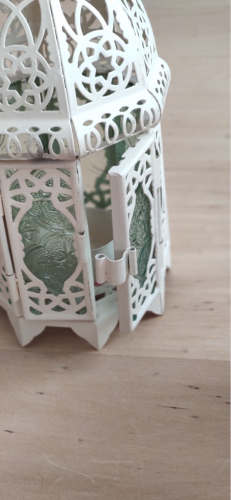 Une lanterne ajourée blanche aux vitres vertes, posée sur une table en bois